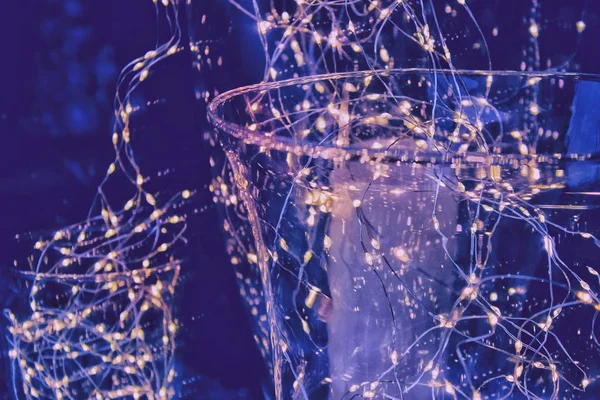 garland lights inside a luxurious glass vase, a festive evening, blue background, glowing warm lights. close-up