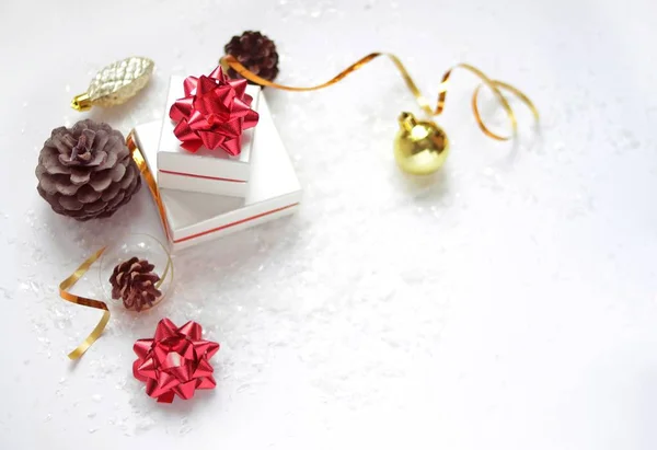 Christmas card. Christmas gift boxes with a red bow, Christmas ball, golden ribbon, cones on a white background with snow and lights