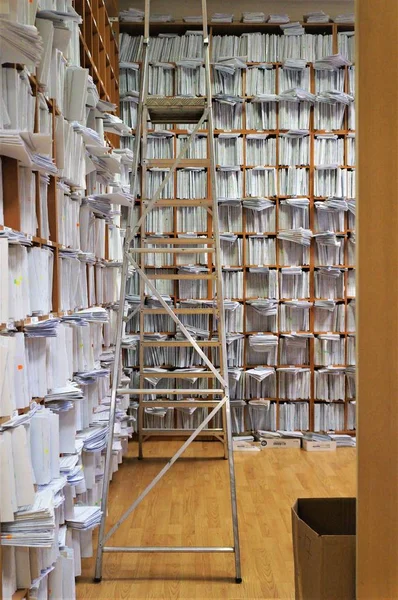 Estantes de madera altos con papeles, por todas las paredes completamente, un depósito de documentos, una escalera de búsqueda en los estantes superiores — Foto de Stock