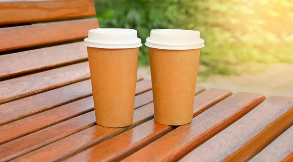 two paper cups with coffee on a bench on a sunny day