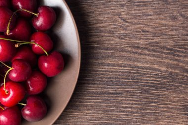 Tahta bir masa üzerinde kahverengi bir tabak üzerinde kırmızı kiraz. Yaz yemeği, sağlıklı beslenme. Organik, vejetaryen, vegan, diyet, diyabetik