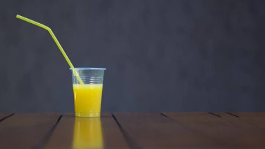 Kahverengi bir arka plan üzerinde bir tüp ile plastik bir Fincan Portakal suyu. Kopya alanı. Piknik, vegan, sağlıklı yiyecek, içecek. Gıda sınıfı plastik lerin yeniden kullanımı ve geri dönüşümü