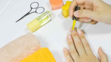 Evde tırnaklarına oje süren bir kadın. Zarif manikür ve oje şişesi olan kadın elleri. Güzellik ve el bakımı konsepti. Evde tırnak bakımı, SPA, güzellik. Uzun doğal tırnaklar. Güzellik salonu