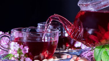 Kırmızı çay, ambar, karkade, Rooibos. Bir kadın fincana çay doldurur. Tören, öğleden sonra çayı, kahvaltı. Çay zamanı, Carcade. Doğulu, samimi, gelenek, Japon, yapraklı, hygge, sonbahar, saat 5 yönünde, kupa