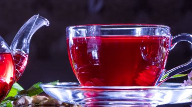 Çay saati: bir fincan çay. Bir fincan amberçiçeği çayı ve çay yapraklarından oluşan yaratıcı bir düzen. Kırmızı çay, carcade, karkade, rooibos. Doğulu, samimi, tören, gelenek, Japon, yapraklı, kızlık zarı, sonbahar, saat 5 yönünde.