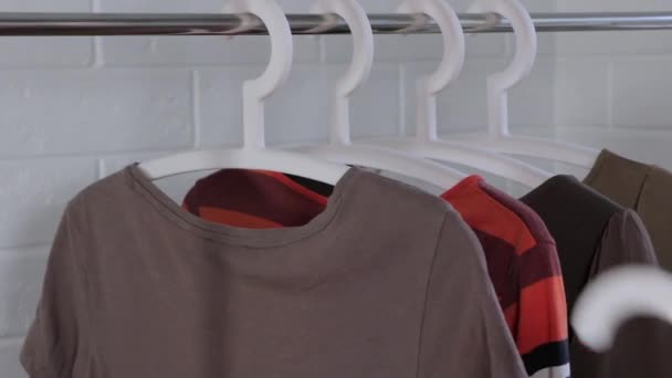 女人从衣架上取下衣服 女人的衣服挂在衣架上 买衣服选择旅行的衣服 打扫衣柜 更衣室 清理内阁 基本衣橱 简约主义 — 图库视频影像