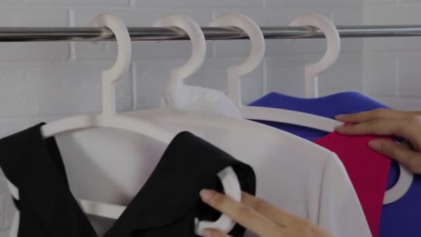 女人选一套衣服 女人的衣服挂在衣架上 经典风格 办公室 买衣服 基本衣橱 简约主义 从衣架上拿件衬衫来 选择一件白色的衬衫 — 图库视频影像