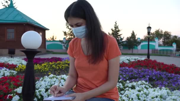 Tıbbi Maskeli Bir Kız Bir Bankta Günlük Tutar Sosyal Uzaklık — Stok video