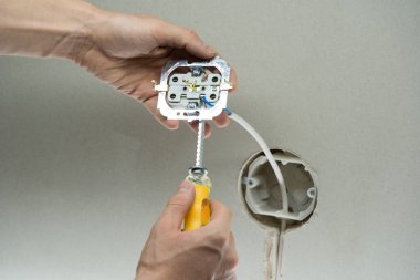 Kabloyu fişe takın. Adamın biri duvara elektrik prizi takıyor. Prizin yanında tornavida tutan teknisyenlere yaklaş. Elektrikçi prizleri elektrik kablolarına bağlıyor.