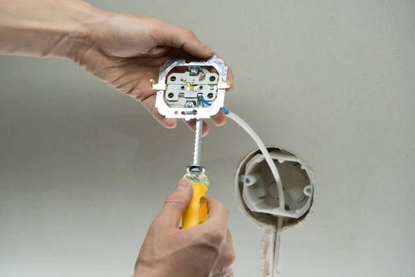 Installation wire into a plug. A man installs an electrical outlet in the wall. Close up of technician holding screwdriver near power socket. Electrician connects the sockets to the electrical wires