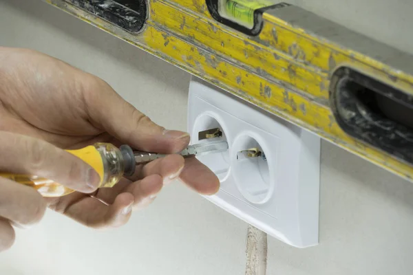 A man installs an electrical outlet in the wall. Close up of technician holding screwdriver near power socket. Electrician connects the sockets to the electrical wires. Installation wire into a plug.