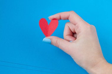 mavi bir arka plan üzerinde kırmızı bir kalp tutan el. Sevgililer günü için arka plan