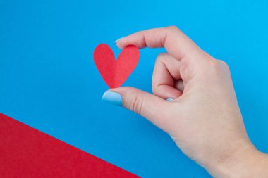 kırmızı ve mavi bir arka plan üzerinde kırmızı bir kalp tutan el. Sevgililer günü için arka plan