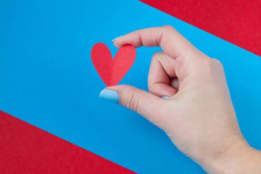 kırmızı ve mavi bir arka plan üzerinde kırmızı bir kalp tutan el. Sevgililer günü için arka plan