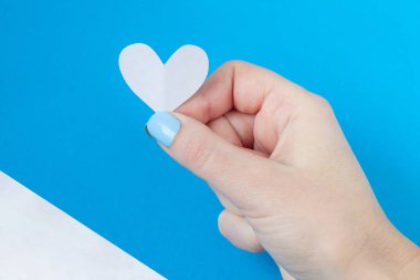 beyaz ve mavi bir arka plan üzerinde beyaz bir kalp tutan el. Sevgililer günü için arka plan