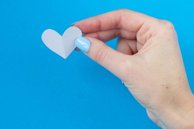 mavi bir arka plan üzerinde beyaz bir kalp tutan el. Sevgililer günü için arka plan