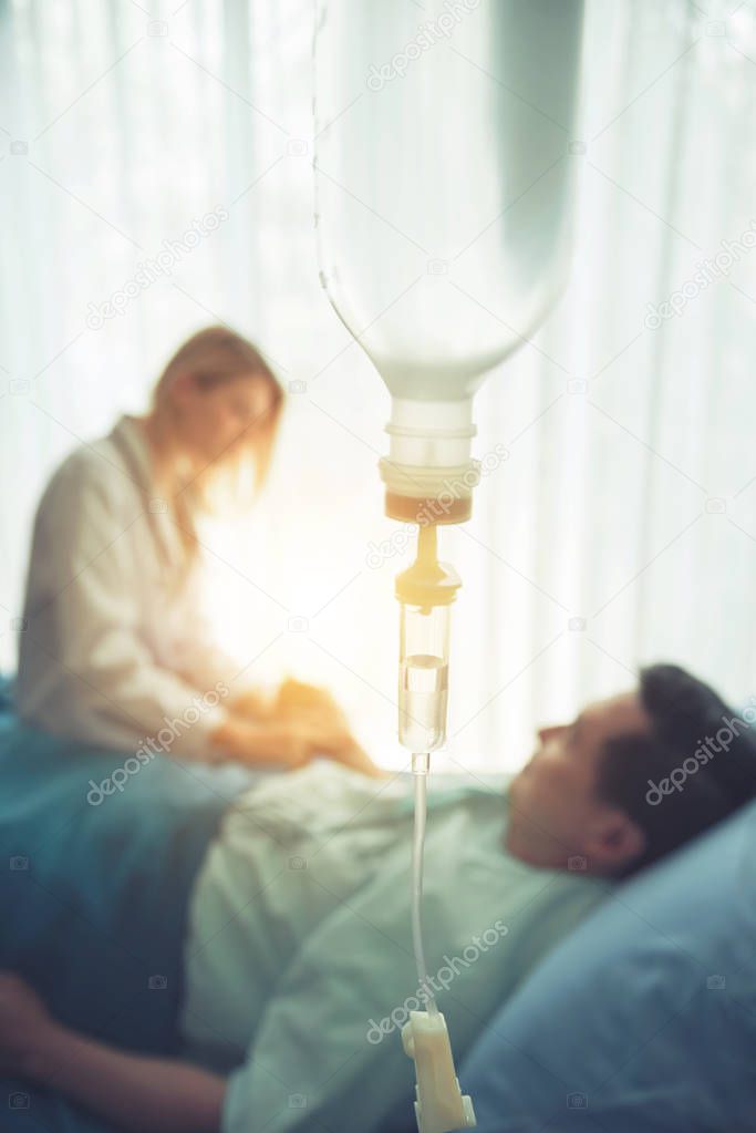 Close up of saline solution dripping with blurred doctor and patient in hospital on background