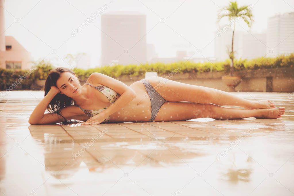 Shapely woman wearing bikini posing near the swimming pool in the rain