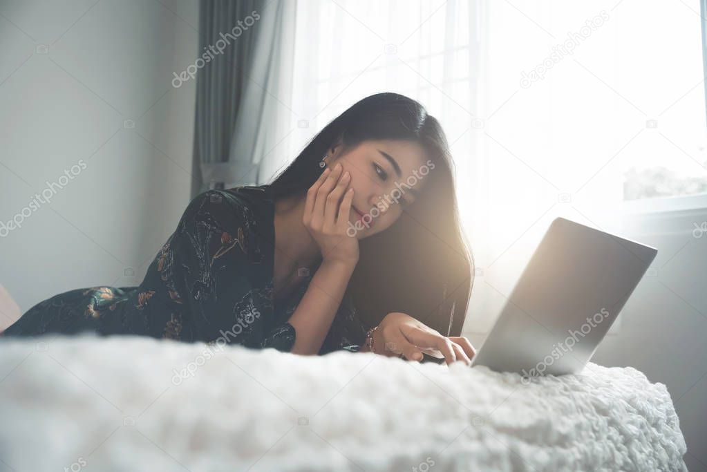 Asian women happy play with laptop on a bed in the room