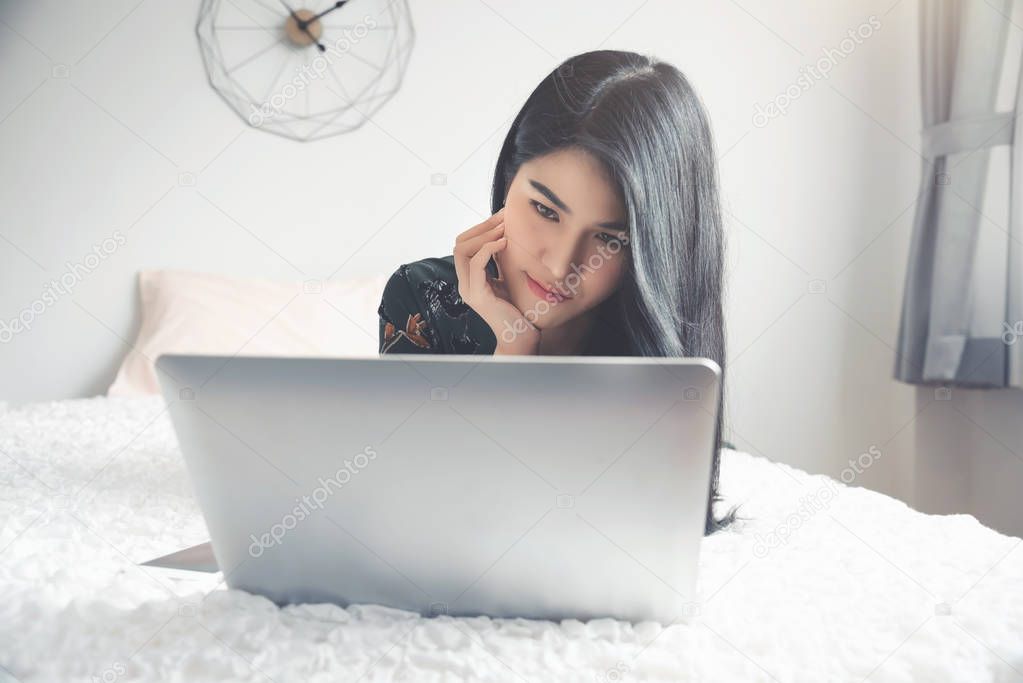 Asian women happy play with laptop on a bed in the room