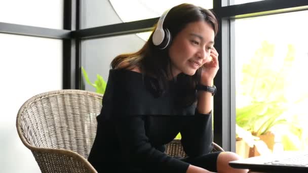亚洲妇女使用笔记本电脑和听音乐与耳机在城市咖啡店 — 图库视频影像