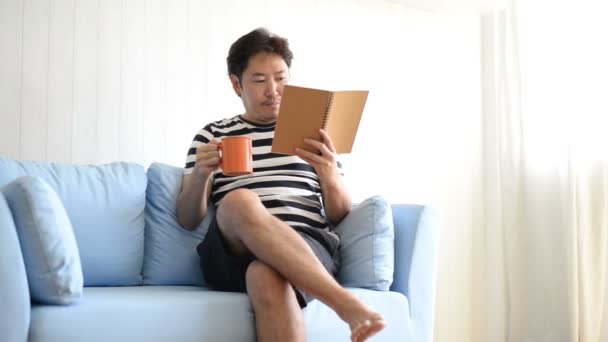 Asiatico Uomo Lettura Libro Bere Caffè Divano Casa — Video Stock