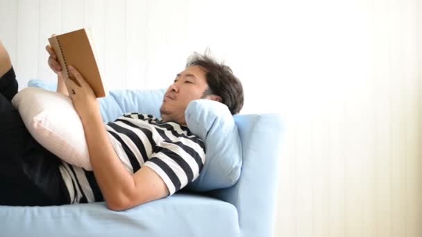 Asian Man Reading Book Lying Sofa — Stock Video