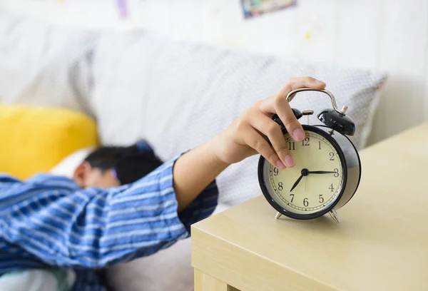 眠そうなアジアの少年 目覚まし時計をオフにベッドから落ちる ロイヤリティフリーのストック写真