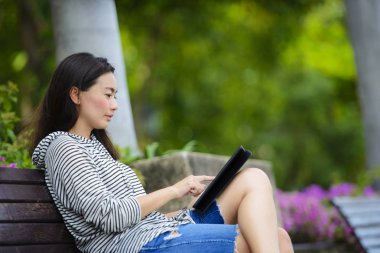 Güzel Asyalı kadın parkta bir bankta tablet bilgisayar kullanarak