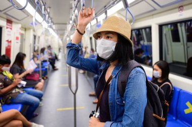 Bangkok metrosunda tek kullanımlık tıbbi maske takan Asyalı kadın.