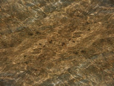 Altta kahverengi kum ile kristal berraklığında suda parlayan dalgalanmalar soyut arka plan.