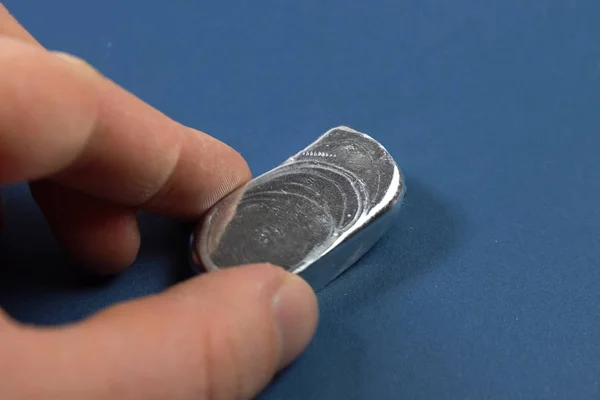 A bar of aluminum in his hand. Spilled aluminum ingot