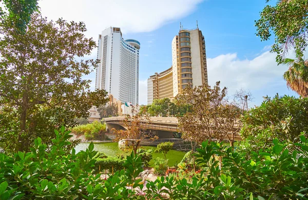 The luxury city hotels and bridge of Abdulaziz Al Saud seen through the lush greenery of riverside garden, Cairo, Egypt.