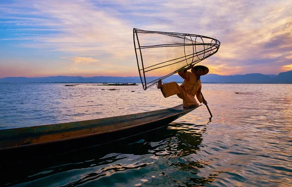 Intha, Myanmar - 18 Şubat 2018: Inle Gölü geleneksel balıkçı pozlar 18 Şubat Intha içinde arka planda, günbatımı gökyüzü ile Kano kenarına koni net ile hüner gösteren,.