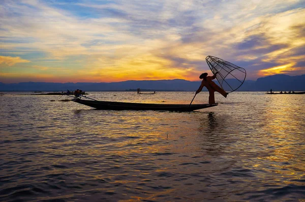 Günbatımı gökyüzü ve bacak kürek balıkçı, Kano'nın yay üzerinde duran ve geleneksel hileler ile net ve kürek, Inle Gölü, Intha, Myanmar gösteren karanlık siluet.