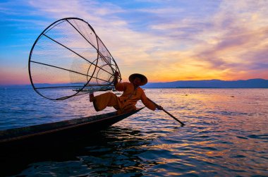 Intha, Myanmar - 18 Şubat 2018: Birmanya balıkçı, hileler net, onun Kano kenarında günbatımı Inle Gölü üzerinde 18 Şubat Intha içinde oturan ile gösterilen karanlık siluet.