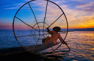 Balıkçı büyük konik net, elle tutarak ve renkli gökyüzü günbatımı ile bacak arka planda, Intha, Inle Gölü, Myanmar gösterilen.