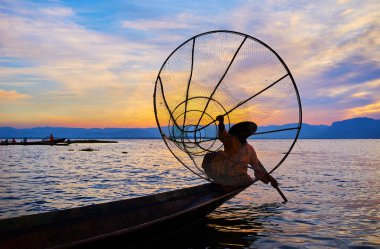 Birman balıkçı kayık kenarında Inle Gölü, Intha, Myanmar üzerinde başka bir el oynamaya siting konik onun net tutar.