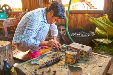 INPAWKHON, MYANMAR - FEBRUARY 18, 2018: The Burmese silversmith at work in traditional workshop-store on Inle lake, on February 18 in Inpawkhon.