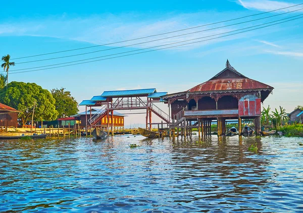 The old wooden stilt houses and scenic foot bridge with canoes, moored under it, Ywama, Inle Lake, Myanmar.