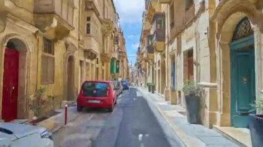 Valletta, Malta - 17 Haziran 2018: Dar boyunca yürüyüş ile korunmuş ortaçağ kilise, Konakları ile St Paul sokak ahşap Malta balkon ve birçok park etmiş arabaların, 17 Haziran'da Valletta renkli. 