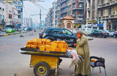 Alexandria, Mısır - 18 Aralık 2017: galabeya (elbise), giyinmiş yaşlı satıcı, ekmek Mahta al Raml eski püskü sepeti gelen tramvay istasyonu'na bitişik kare üzerinde Aralık 18 Alexandria satıyor.