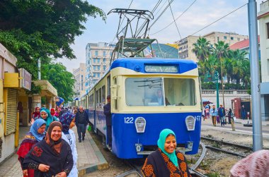 ALEXANDRIA, EGYPT - DECEMBER 18, 2017: The crowd on a tram station at the vintage blue tram of Al Ramlh tramway system, Mahta Al Raml square, on December 18 in Alexandria. clipart
