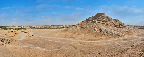 Panorama of rocky desert grounds of Dakhma Zoroastrian complex, preserved Tower of Silence located on hilltop and numerous Khaiele ritual buildings at the foot of the hill, Yazd, Iran.