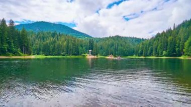 Pitoresk Synevyr Gölü iğne yapraklı ormanlar ve Karpat Dağları ile çevrili, açık yüzey hızlı akan bulutlar yansıtır, turistler ahşap cankurtaran, Ukrayna gezisinde zevk.