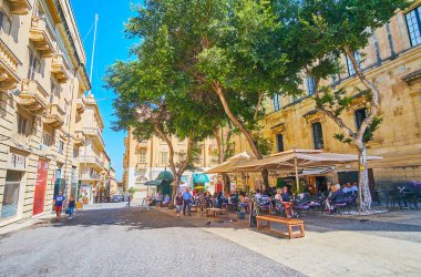 VALLETTA, MALTA - JUNE 17, 2018: The cozy outdoor cafe is hidden in shade of trees in St John street, on June 17 in Valletta. clipart