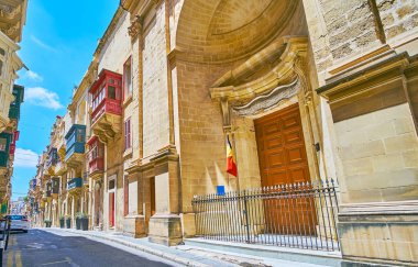 Ensemble of medieval St Ursula street includes the Baroque Church of St Roque and traditional edifices with bright Maltese balconies, Valletta, Malta. clipart