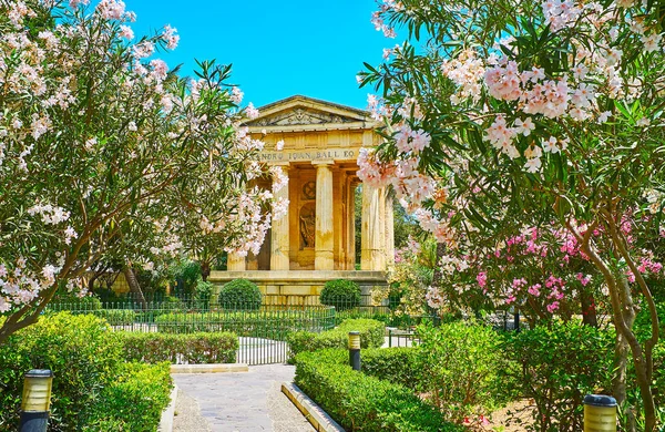 The narrow path in Lower Barrakka Gardens is lined with blooming rhododendron plants and leads to the monument, styled as the antique temple, Valletta, Malta.