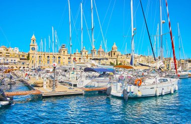 Birgu, Malta - 17 Haziran 2018: Beyaz yelken yat Tersanesi Vittoriosa (Birgu) Marina, Deniz Müzesi, saat kulesi ve kubbe St Lawrence Kilisesi arka planda, 17 Haziran'da Birgu olarak görülür, demirlemiş hattı.