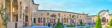 KASHAN, IRAN - OCTOBER 22, 2017: Panorama of Tabatabaei House and its pleasant garden with tiny trees, flower beds and fountains, amid the ornate walls and terraces, on October 22 in Kashan. clipart